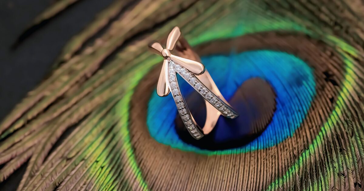 A warm rose gold diamond ring resting on an iridescent peacock feather